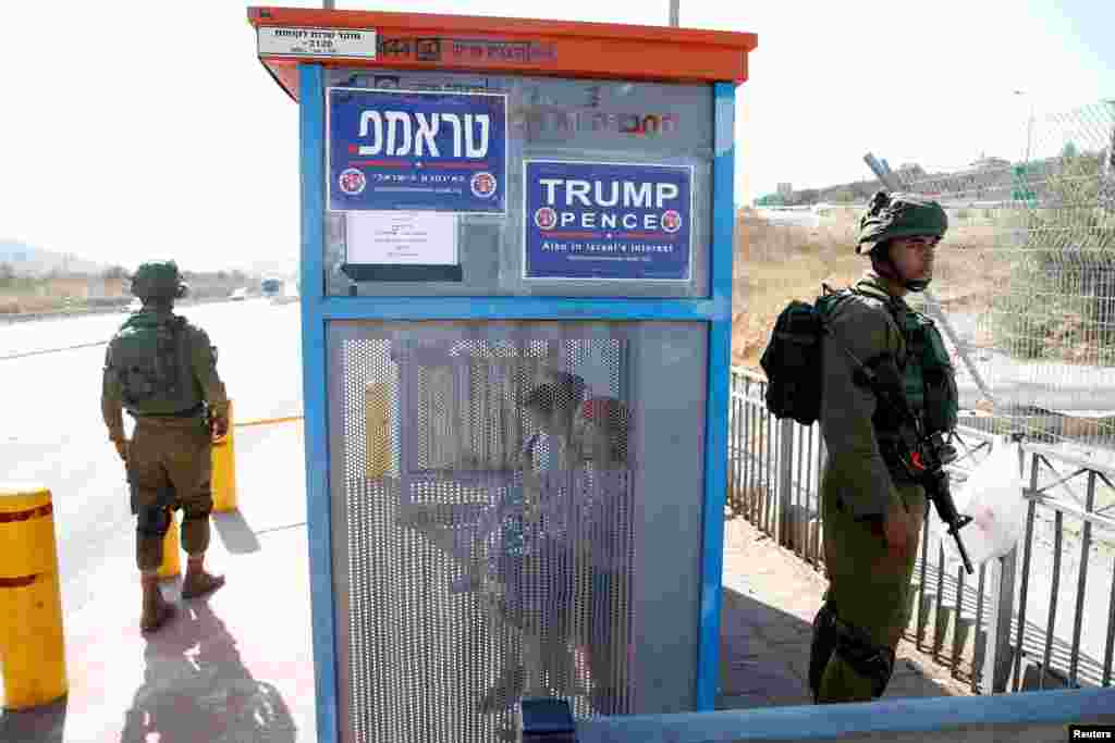 Israeli soldiers are seen next to a bus stop covered with posters from the Israeli branch of the U.S. Republican party campaign in favor of Donald Trump, near the West Bank Jewish Settlement of Ariel.