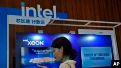 FILE - A woman checks her smartphone near an Intel booth promoting Xeon chips during a tech summit in Beijing, Aug. 16, 2023. 