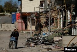 Arhiva - Čovek gura bicikl duž trgovačke ulice uništene u ruskim napadima, u gradu Kupjansk, Ukrajina, 18. oktobra 2022.
