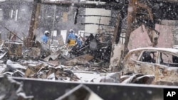 Salju turun saat petugas polisi melanjutkan operasi pencarian di sekitar pasar yang terbakar di Wajima usai gempa, prefektur Ishikawa, Jepang, 7 Januari 2024. (Foto: Kyodo via AP)