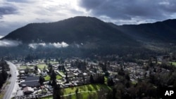 A vehicle at left drives down Rogue River Highway as light shines on the area, March 23, 2024, in Grants Pass, Ore. 