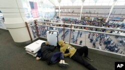 Dua orang pelancong tidur di bandara sementara para pelancong lainnya antre melewati pos pemeriksaan keamanan di Bandara Internasional Denver saat badai musim dingin melanda AS, 23 Desember 2022.