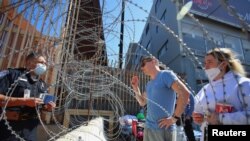 Seorang petugas perbatasan AS mendengarkan beberapa warga Rusia yang tengah berusaha mendapatkan visa kemanusiaan di lokasi gerbang masuk San Ysidro di perbatasan AS-Meksiko di Tijuana, Meksiko, pada 15 Maret 2022. (Foto: Reuters/Jorge Duenes)
