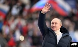 Vladimir Putin mokonzi ya Russie atamboli loboko na lisikulu lya ye liboso lya bituluku na bato na stade Luzhniki, Moscou, 18 mars 2022