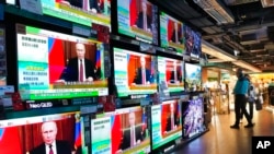 Tampak beberapa orang berdiri di dekat layar televisi yang menayangkan berita invasi Rusia ke Ukraina di sebuah pusat perbelanjaan di Hong Kong, pada 24 Februari 2022. (Foto: AP/Vincent Yu)