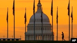 Siluet pejalan kaki dberjalan melewati bendera AS di National Mall dan melewati US Capitol Building di Washington, 7 November 2022. (Foto: AP)