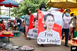 រូបឯកសារ៖ អ្នក​តវ៉ា​ដើរ​កាត់​ផ្សារ​មួយ​ដែល​មាន​ផ្ទាំង​រូបភាព​មេដឹកនាំ​មីយ៉ាន់ម៉ា​អ្នកស្រី Aung San Suu Kyi​នៅ​សង្កាត់ Kamayut ក្នុង​ទីក្រុង Yangon ប្រទេស​មីយ៉ាន់ម៉ា កាល​ពី​ថ្ងៃ​ព្រហស្បតិ៍ ទី ៨ ខែ​មេសា ឆ្នាំ ២០២១។