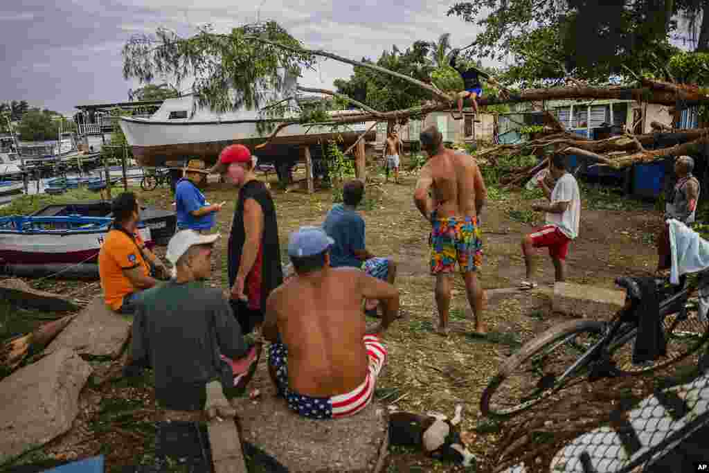 Residents watch as a person chops on a tree that fell on top of a boat due to Hurricane Ian in Havana, Cuba, Sept. 28, 2022.