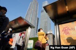 Warga memakai masker menunggu di halte bus dekat gedung pencakar langit di Central Business District di Beijing, Senin, 24 Oktober 2022. (Foto: AP)