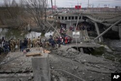 Orang-orang menyeberang di jalur improvisasi di bawah jembatan yang dihancurkan oleh serangan udara Rusia, saat melarikan diri dari kota Irpin, Ukraina, 5 Maret 2022. (Foto: AP)