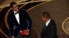 Presenter Chris Rock, left, reacts after being hit on stage by Will Smith while presenting the award for best documentary feature at the Oscars on Sunday, March 27, 2022