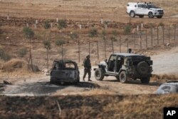 Tentara Israel berjalan dengan mobil yang terbakar yang dilaporkan digunakan oleh orang-orang bersenjata Palestina di dekat lokasi serangan penembakan di sebuah bus Israel, di Lembah Yordan Tepi Barat, Minggu, 4 September 2022. (AP/Mahmoud Illean)