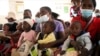 Women holding babies take their places on wooden benches at a clinic in Harare, Zimbabwe, Thursday, Sept. 15, 2022. 