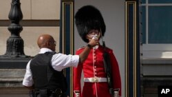 A police officer givers water to a British soldier wearing a traditional bearskin hat, on guard duty outside Buckingham Palace, during hot weather in London, July 18, 2022.