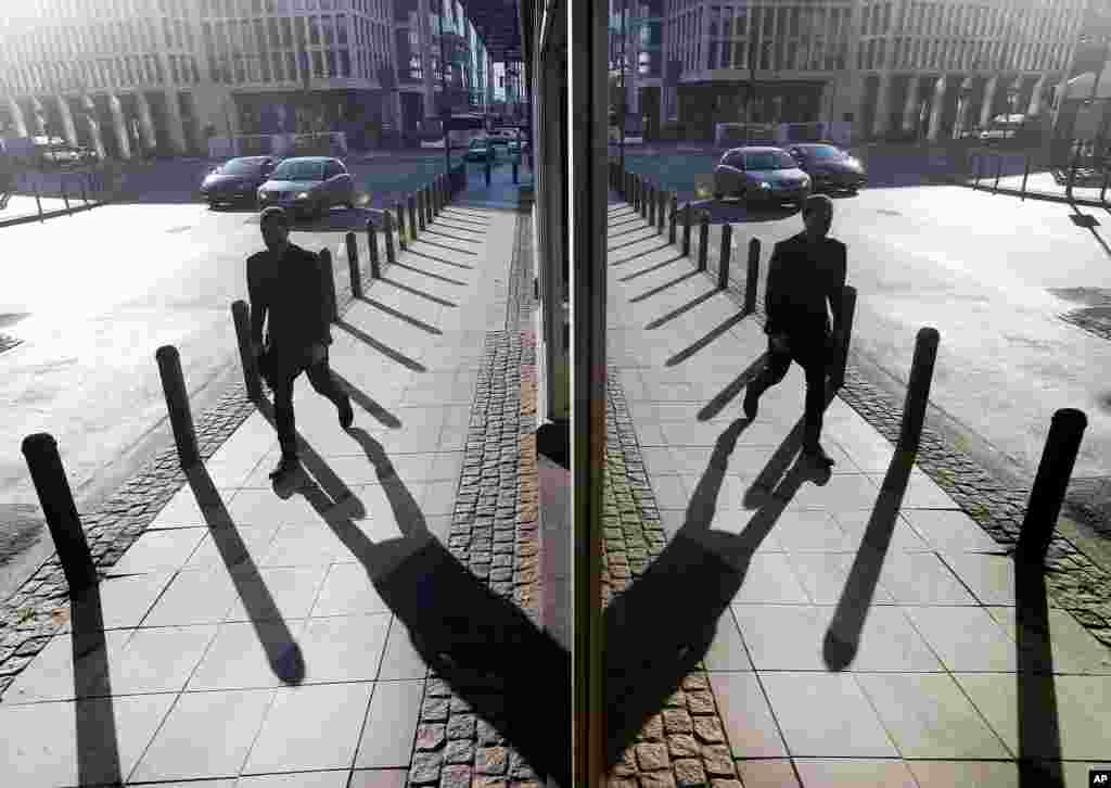 A businessman, rushing to work, is reflected in a window as the sun comes up in downtown Frankfurt, Germany.
