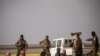 U.S.-backed Syrian Democratic Forces stand guard over men suspected of being Islamic State (IS) group fighters at a screening point outside Baghuz in eastern Syria, March 6, 2019.