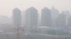 FILE - Suasana di sebuah lokasi pembangunan di Beijing, China, dengan latar belakang gedung pencakar langit berselimut kabut tebal akibat polusi udara yang parah, 11 Maret 2021.