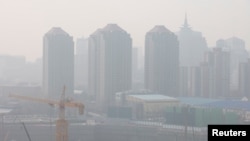 FILE - Suasana di sebuah lokasi pembangunan di Beijing, China, dengan latar belakang gedung pencakar langit berselimut kabut tebal akibat polusi udara yang parah, 11 Maret 2021.