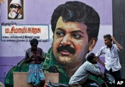 FILE - People stand in front of a mural of Sri Lanka's Liberation Tigers of Tamil Eelam (LTTE) leader Velupillai Prabhakaran painted on a wall in Chennai, India, May 19, 2015. Across Chennai, large billboards with photographs of Prabhakaran, the leader of the Tamil Tigers, urge its people to "not forget" the day the insurgent group accepted defeat.