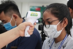 Seorang jurnalis Kamboja (kanan), diperiksa suhu badannya saat akan meliput upacara penyerahan donasi di Phnom Penh, Kamboja, Sabtu, 28 Maret 2020. (Foto: dok).