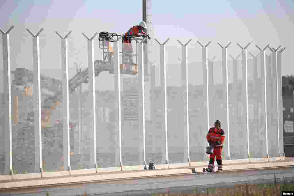 Workers set up barbed-wire atop a fence along the harbor of Calais to prevent migrants from jumping aboard lorries, in France.