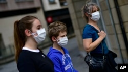 A family wearing face mask to protect of the coronavirus go for a walk, in Pamplona, northern Spain, Sunday, April 27, 2020. On Sunday, children under 14 years old will be allowed to take walks with a parent for up to one hour and within one…