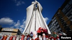 Lilin dan bunga yang dihias diletakkan di samping patung mendiang Paus Yohanes Paulus II di luar Rumah Sakit Gemelli Roma, tempat Paus Fransiskus dirawat karena pneumonia, Sabtu, 22 Februari 2025. (Foto: Vincenzo Livieri/Reuters)
