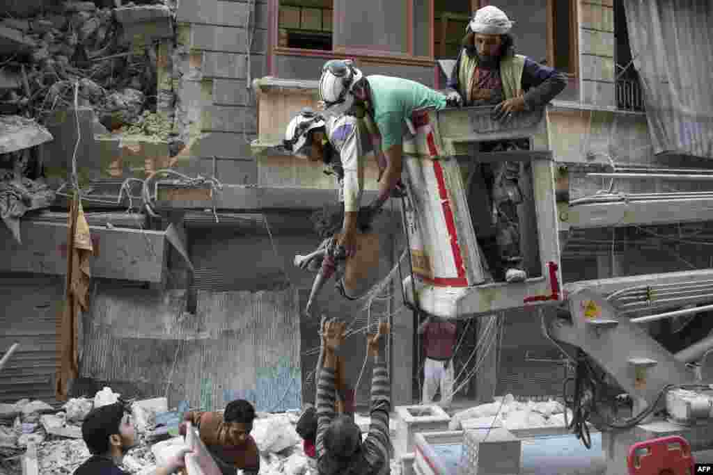 Syrian rescuers hand down the body of a girl to civilians on the ground after she was pulled from the rubble of a building following airstrikes by government forces in the rebel-held neighborhood of Al-Shaar in Aleppo.