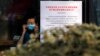 A woman puts on a mask near a notice board that reads "Bans on wild animals trading following the coronavirus outbreak" at a cafe in Beijing, Monday, Feb. 10, 2020.