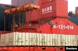 FILE - A worker gestures as a crane lifts goods onto a cargo ship, at a port in Lianyungang, Jiangsu province, China, May 31, 2018.