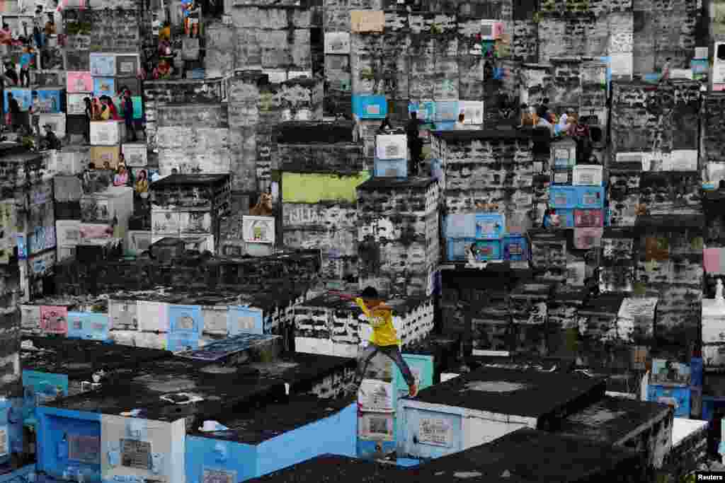 A boy leaps in-between apartment-style tombs as Filipinos visit the graves of their deceased loved ones to commemorate All Saints Day, at Barangka public cemetery in Marikina city, Metro Manila.
