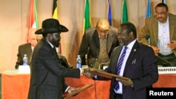 South Sudan's President Salva Kiir (front L) and South Sudan's rebel commander Riek Machar exchange documents after signing a cease-fire agreement during the Inter Governmental Authority on Development (IGAD) Summit on the case of South Sudan in Ethiopia'