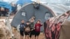 FILE - Children look on as they stand next to a tent at a flooded camp for Syrians displaced by conflict near the village of Kafr Uruq, in Syria's northern rebel-held Idlib province, Jan. 17, 2021. 