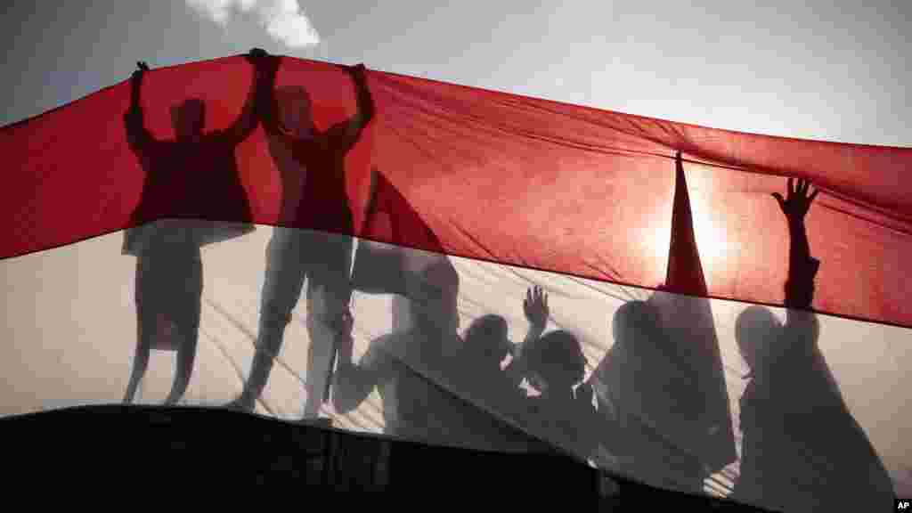 Men are silhouetted against a large representation of the Yemeni flag as they attend a ceremony to mark the 54th anniversary of North Yemen's revolution in Sana'a.