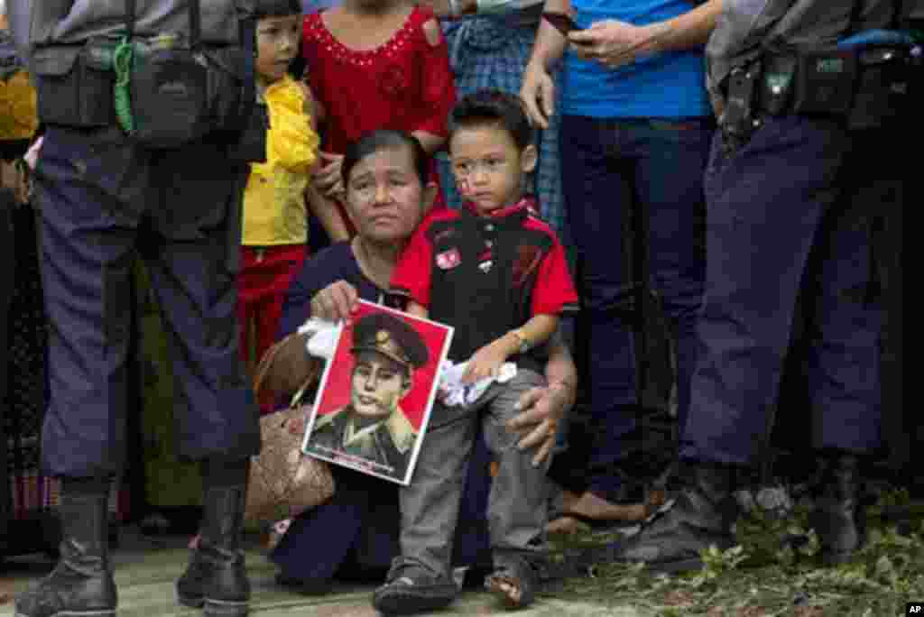 A woman holds a portrait of Gen. Aung San at a barricade leading to Martyrs' Mausoleum in Yangon, Myanmar, Sunday, July 19, 2015. Hundreds of people gathered to pay respect at the tomb of Myanmar's Independence hero and opposition leader Aung San Suu Kyi