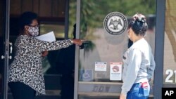 FILE - A masked worker at a state job center holds an unemployment benefit form as she directs an applicant, in Pearl, Mississippi, April 21, 2020.