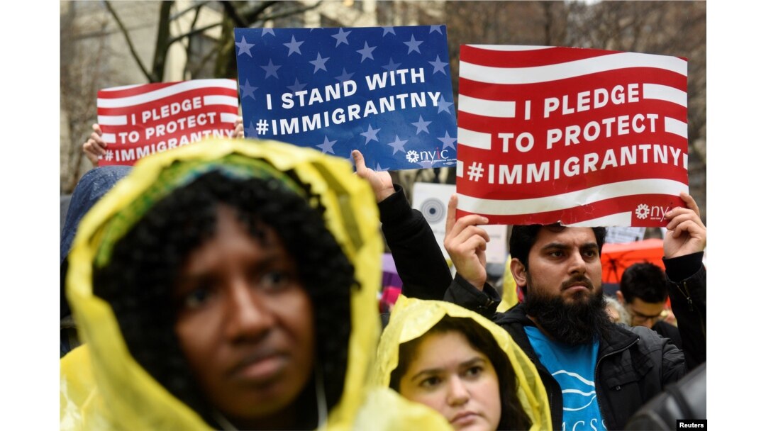 FILE - People hold signs before marching to Trump Tower in a protest organized by the New York Immigration Coalition against President-elect Donald Trump in New York, Dec. 18, 2016.