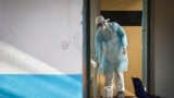 Un travailleur médical portant un équipement de protection complet décontamine une tasse utilisée par un homme mis en quarantaine après être entré en contact en Ouganda avec un porteur du virus de Marburg, au Kenya, le 8 octobre 2014 (AP/Ben Curtis)