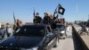 FILE - Islamic State militants pass by a convoy in Tel Abyad town, northeast Syria.