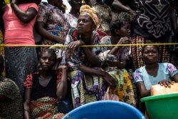 FILE - A woman looks on while people wait for their ration of food to be handed out at a food distribution Oct. 25, 2017 in Kasala, in the restive province of Kasai, Democratic Republic of Congo.