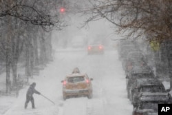 Seorang pria membersihkan jalanan dari salju dengan menggunakan sekop di tengah lalu lintas di 81st street, 4 Januari 2018, di Upper East Side, Manhattan.