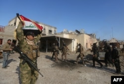 FILE - A member of the Iraqi security forces raises the Iraqi flag in the Anbar police headquarters after their entry into the center of Ramadi, Dec. 28, 2015.