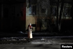 Seorang perempuan berdiri di pinggir jalan sambil diterangi lampu mobil menyusul serangan Rusia terhadap fasilitas energi Ukraina di tengah serangan Rusia ke Ukraina, di pusat Kyiv, Ukraina, Jumat, 13 Desember 2024. (Foto: Thomas Peter/Reuters)