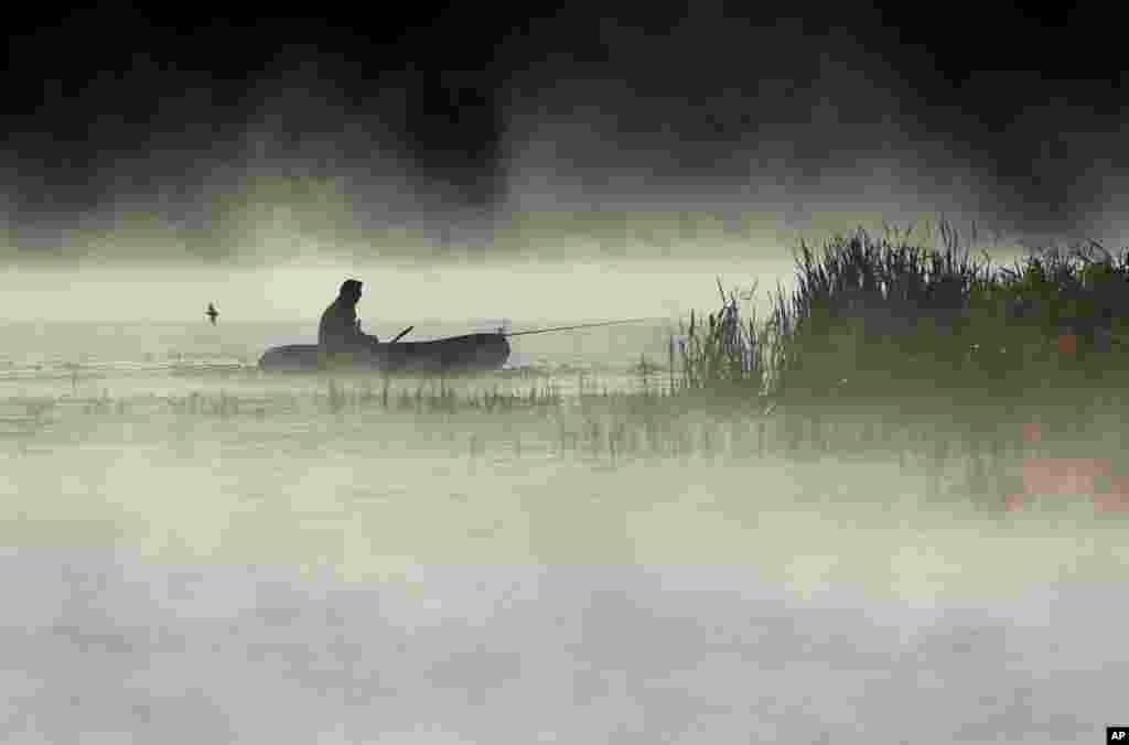 A man fishes from his boat as fog rises over the lake in the town of Logoisk, 40 kms. (25 miles) north of Minsk, Belarus.