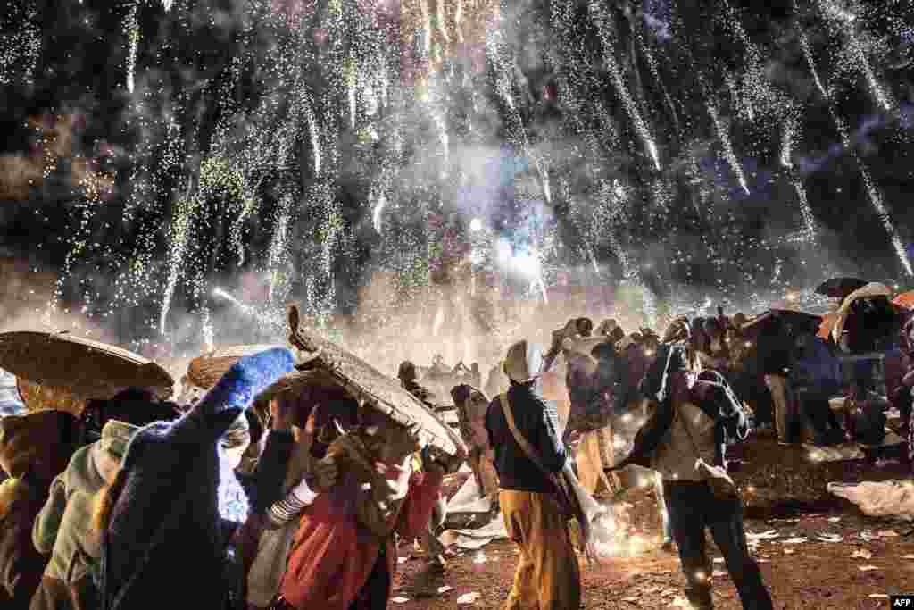 People protecting themselves from fireworks, being carried by a hot air balloon during the Tazaungdaing Lighting Festival at Taunggyi in Myanmar's northeastern Shan State, Nov. 12, 2016.