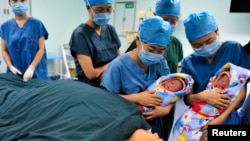 Perawat menunjukkan sepasang saudara kembar kepada ibu mereka (bawah) setelah mereka lahir di pusat bayi tabung sebuah rumah sakit di Xi'an, Provinsi Shaanxi. Foto: Reuters)