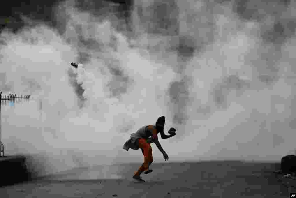 A Kashmiri demonstrator throws a tear smoke shell on government forces to protest against the Sunday's killing of a young man in Srinagar, Indian-controlled Kashmir.