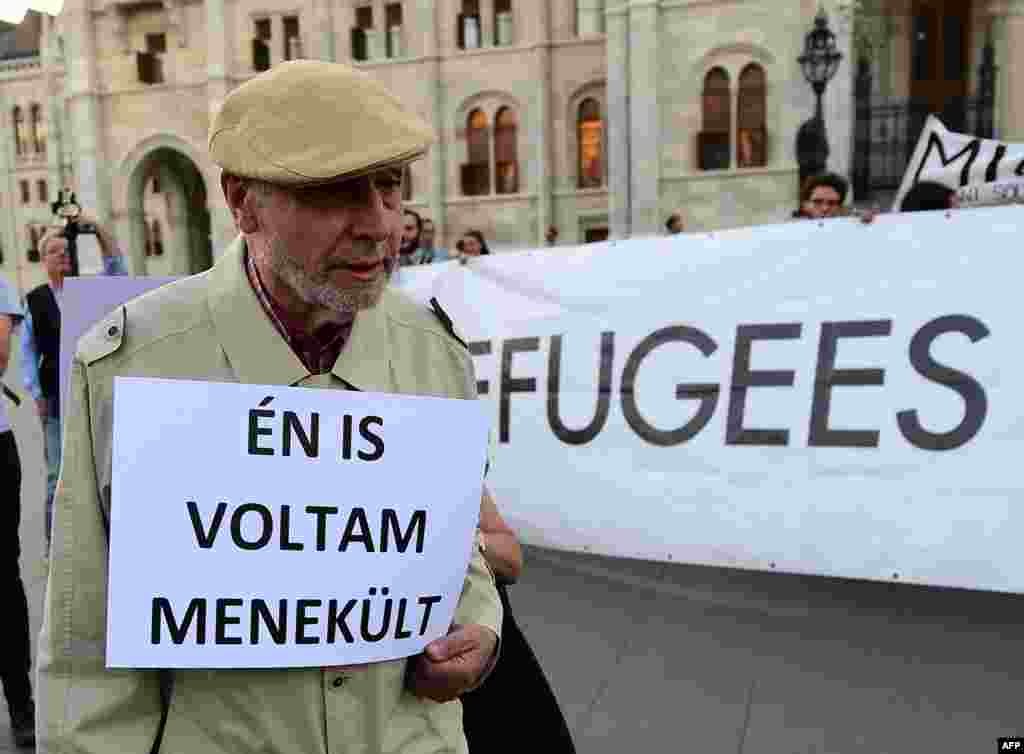 An elderly man walks with his placard with text, "I was refugee also," as activists hold up a banner with 'Refugees welcome' during protests against the migration policy of the Orban government in front of the parliament building in Budapest. A referendum on the EU's migrant resettlement plans will be held on Sunday in Hungary.