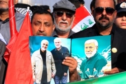 FILE - Supporters of the PMF hold a poster of Abu Mahdi al-Muhandis, of the Popular Mobilization Forces, and General Qassem Soleimani, head of Iran's Quds force, during a rally to commemorate their deaths, in Basra, Iraq, Jan. 8, 2021.