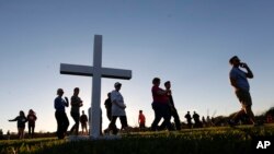 Para peserta melewati sebuah salib kayu saat mereka tiba pada acara penyalaan lilin sebagai bentuk solidaritas bagi para korban penembakan di SMA Marjory Stoneman Douglas di Parkland, Florida, 15 Februari 2018 (Foto: AP Photo/Wilfredo Lee)